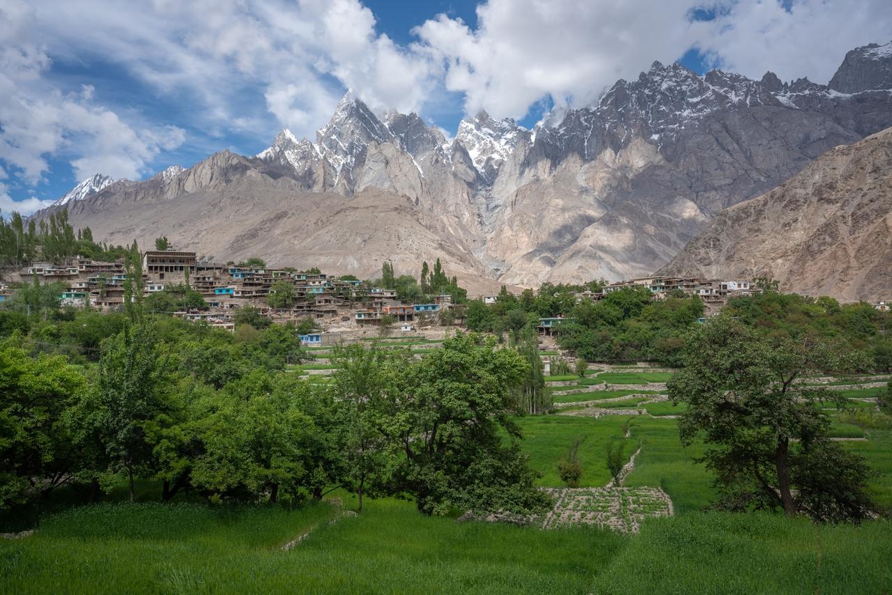 Green terraced fields and a mountain village beneath snow-capped peaks in northern Pakistan